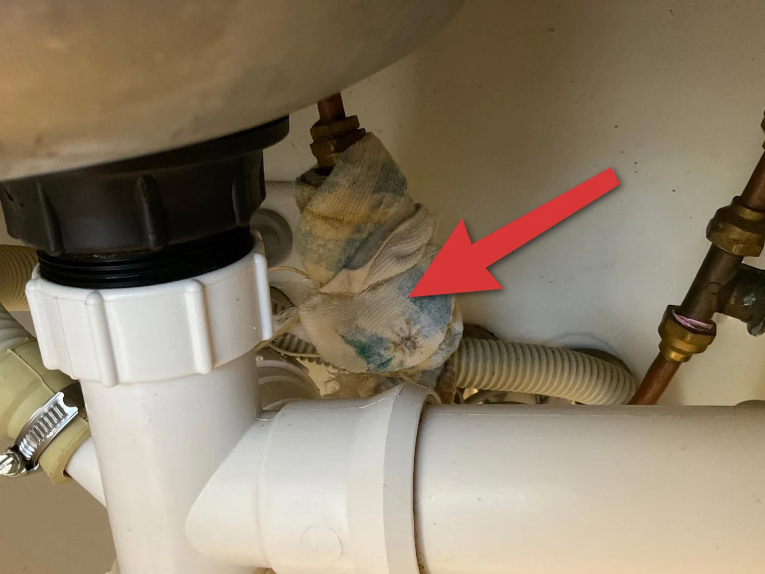 Rag wrapped around a leaking pipe joint under a kitchen sink as a makeshift repair