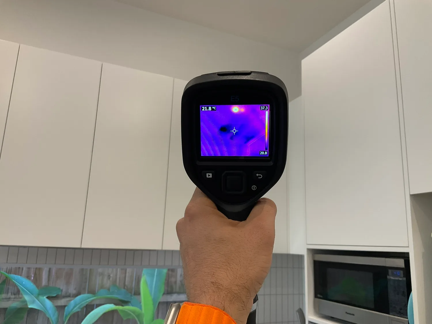 Owner Inspections inspector using a thermal imaging camera to detect hidden moisture behind kitchen cabinetry