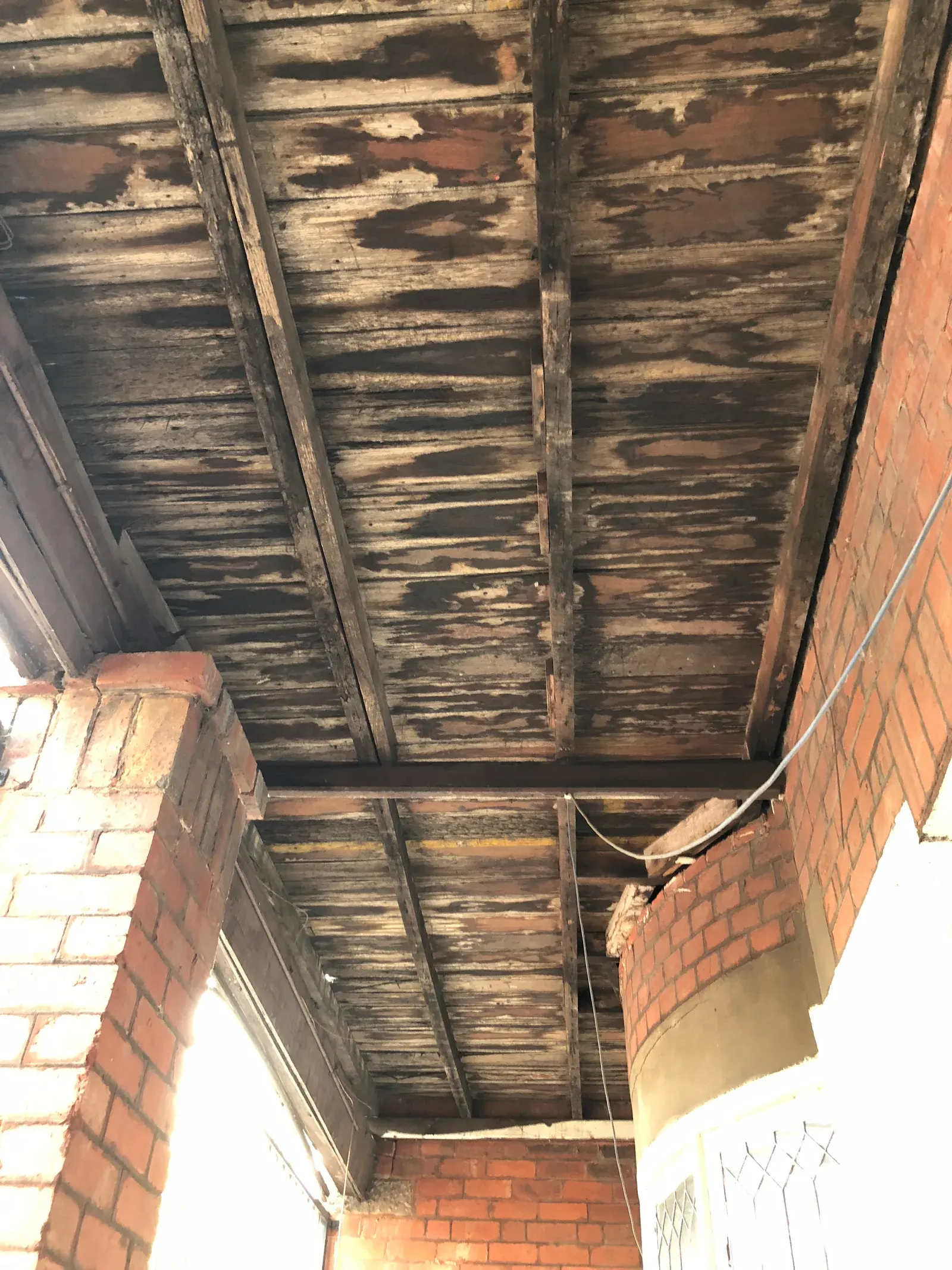 Water staining spread across timber ceiling boards and joists exposed after a long running leak from above