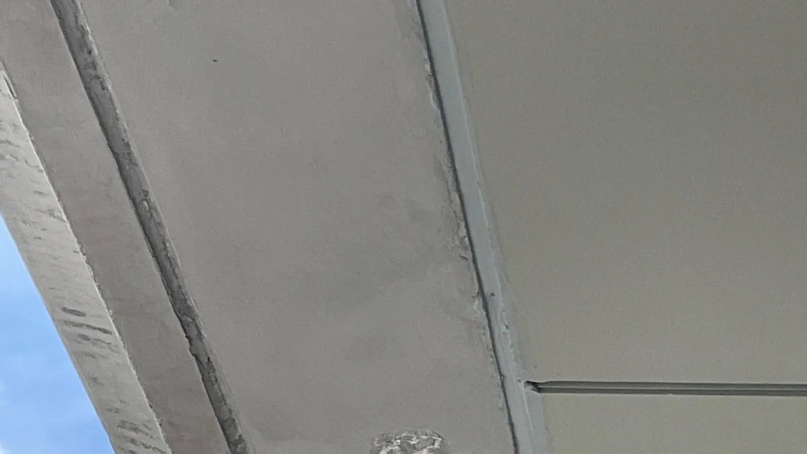 Underside of a concrete balcony slab with a faint stained patch and a flaking spot beside a painted soffit panel joint