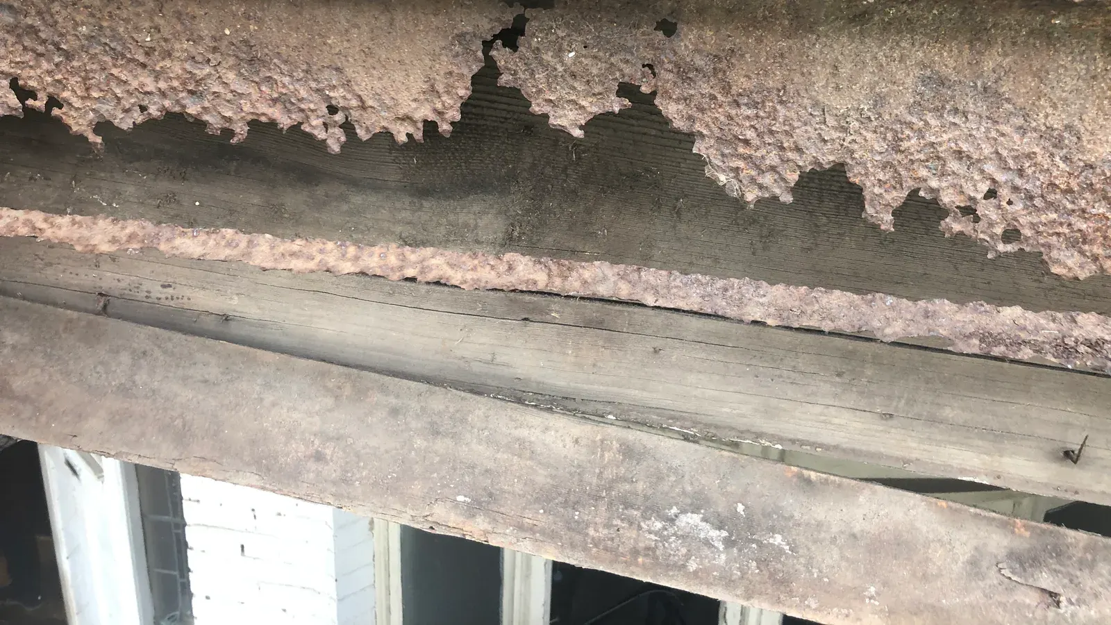 Severely corroded steel lintel with delaminating rust sitting over timber framing, photographed during a defect investigation