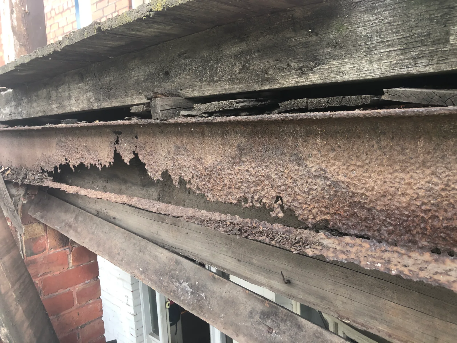 Severely corroded steel lintel with delaminating rust layers lifting decayed timber above it