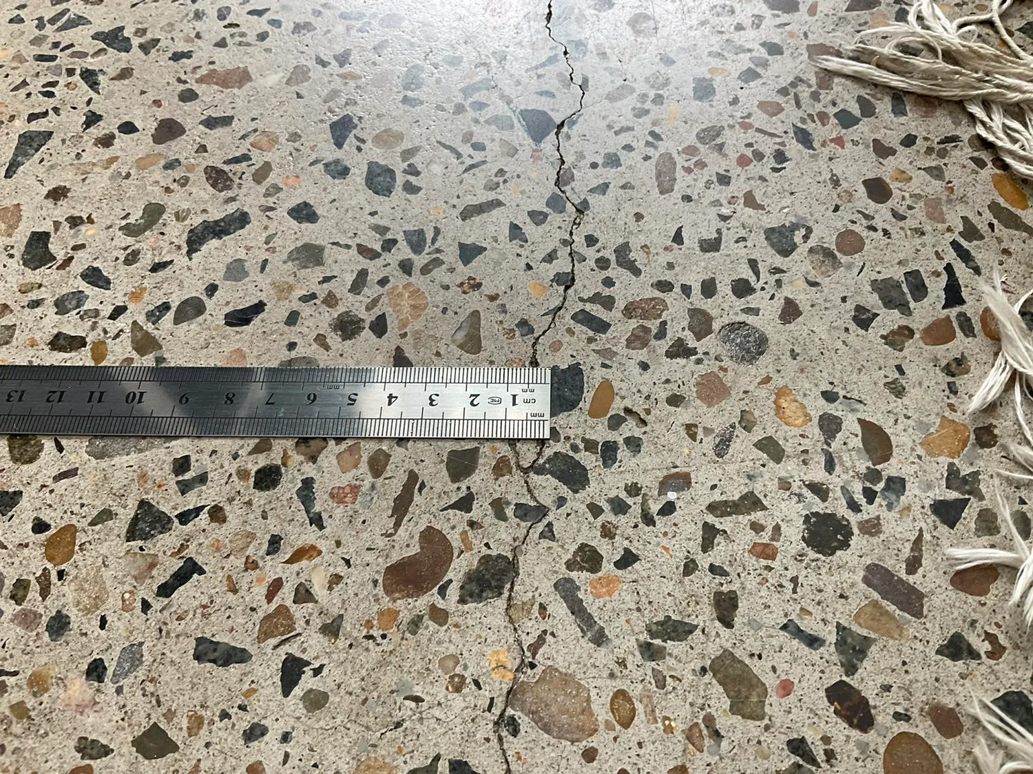 Inspector measuring the width of a crack in a concrete slab with a steel rule during an insurance claim assessment
