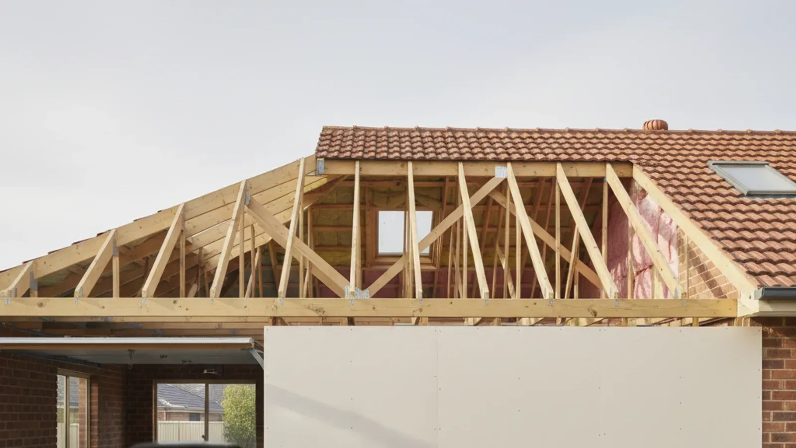 Plasterboard garage wall stopping at ceiling level with the timber roof truss space above it open and continuous into the house roof