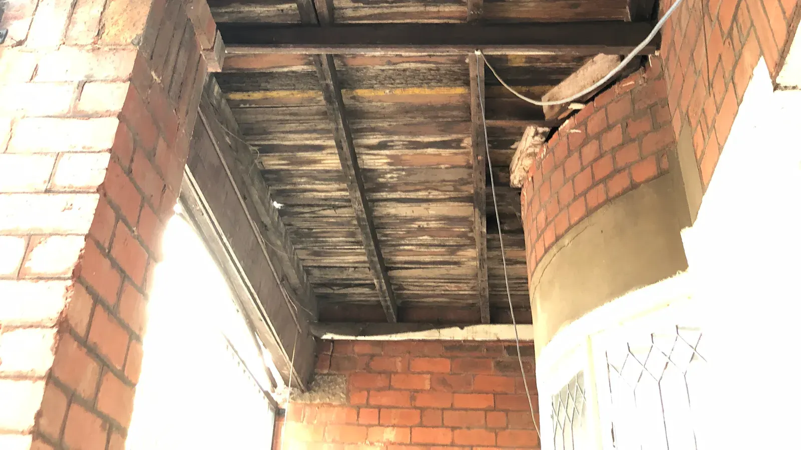 Ceiling joists and timber boards exposed after linings were removed during a renovation, showing dark staining and deterioration