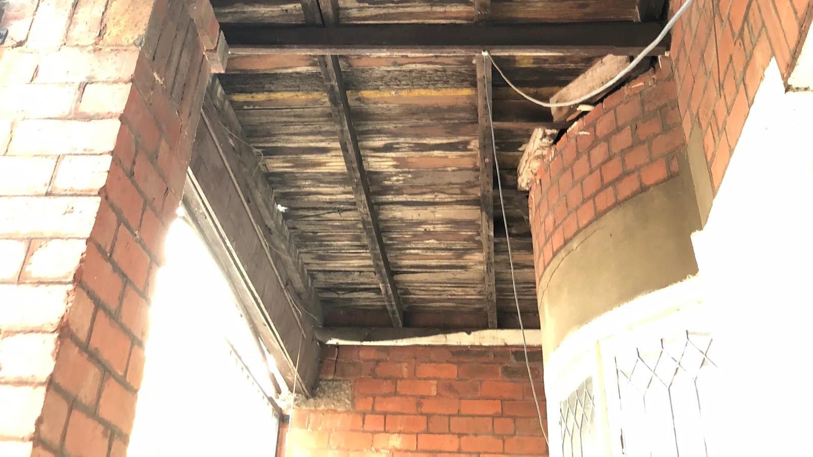 Structural floor timbers and boards exposed after linings were removed, showing dark deterioration and loss of surface along the members