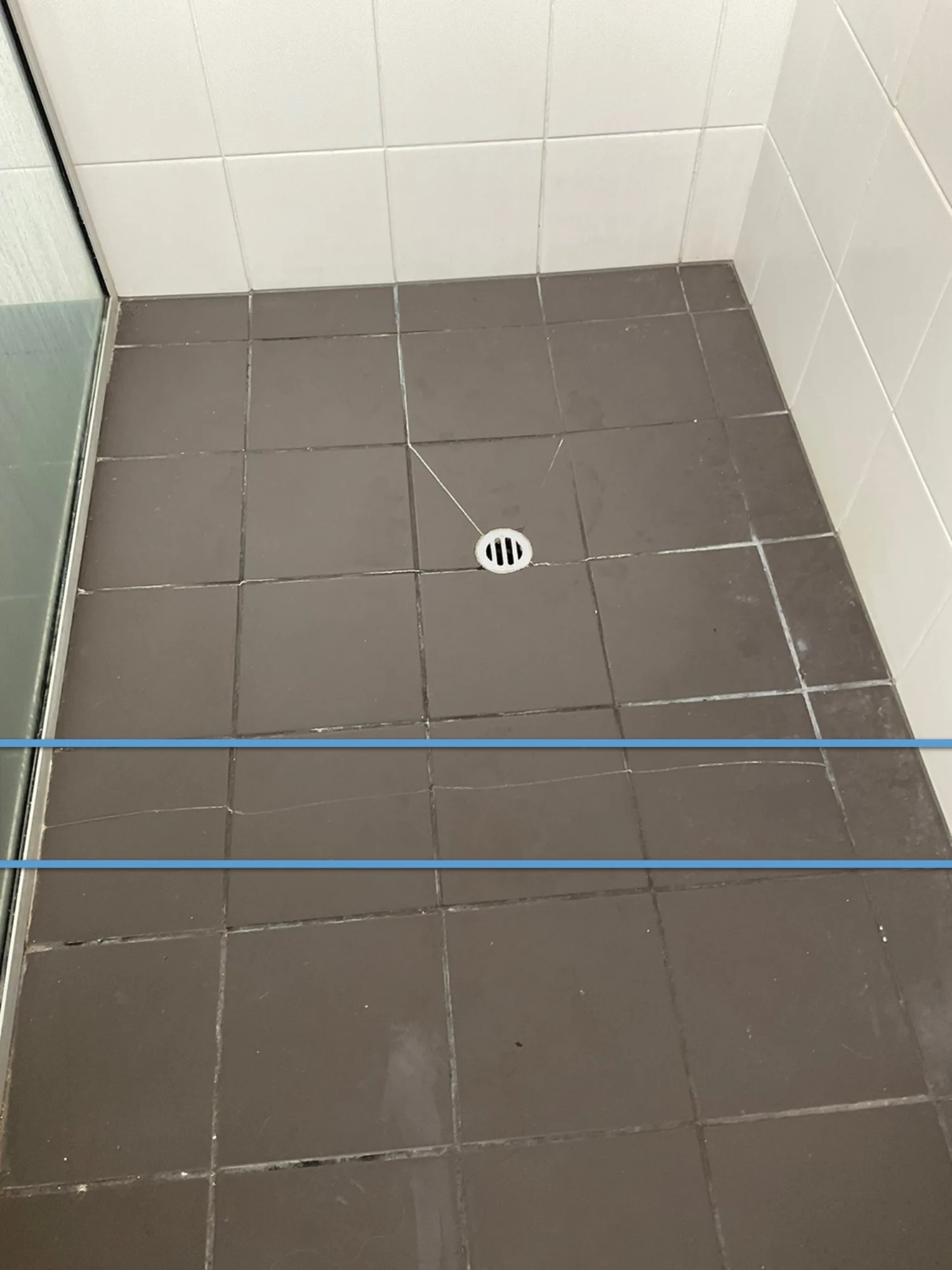 Cracked bathroom floor tiles radiating from a shower floor waste, marked with level lines during an inspection