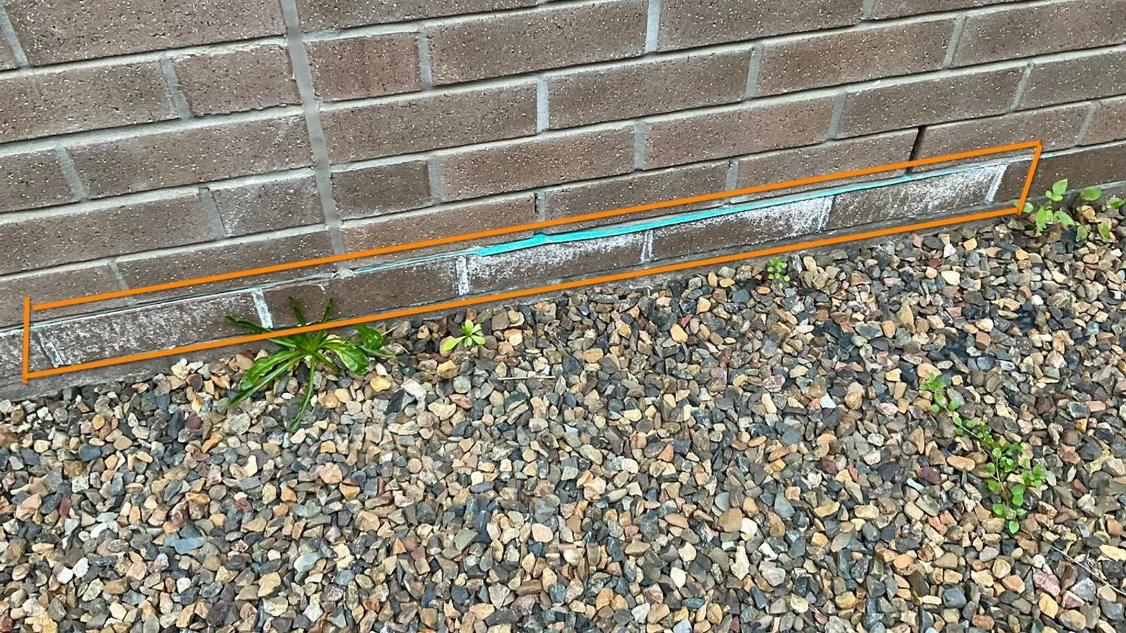 Patched mortar repair at the base of a brick wall marked up during a pre-settlement inspection
