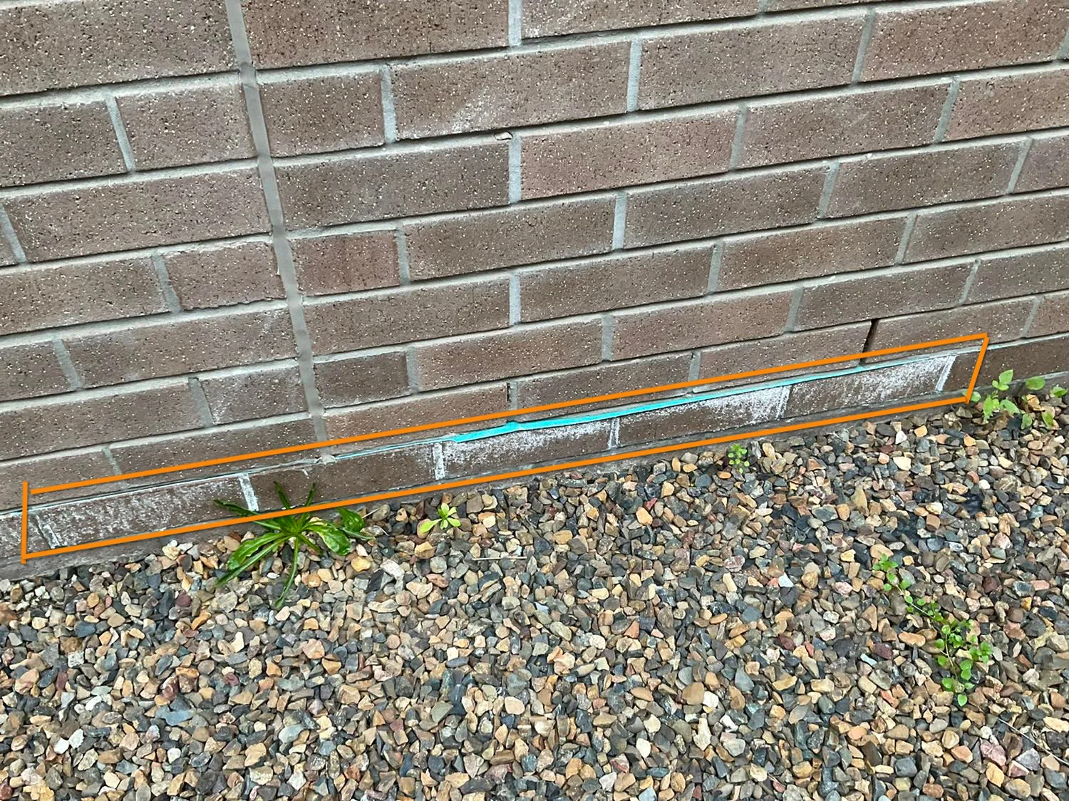 Gravel built up against the base of a brick wall, flagged during an inspection because it sits over the bottom course where weep holes and the damp-proof course are