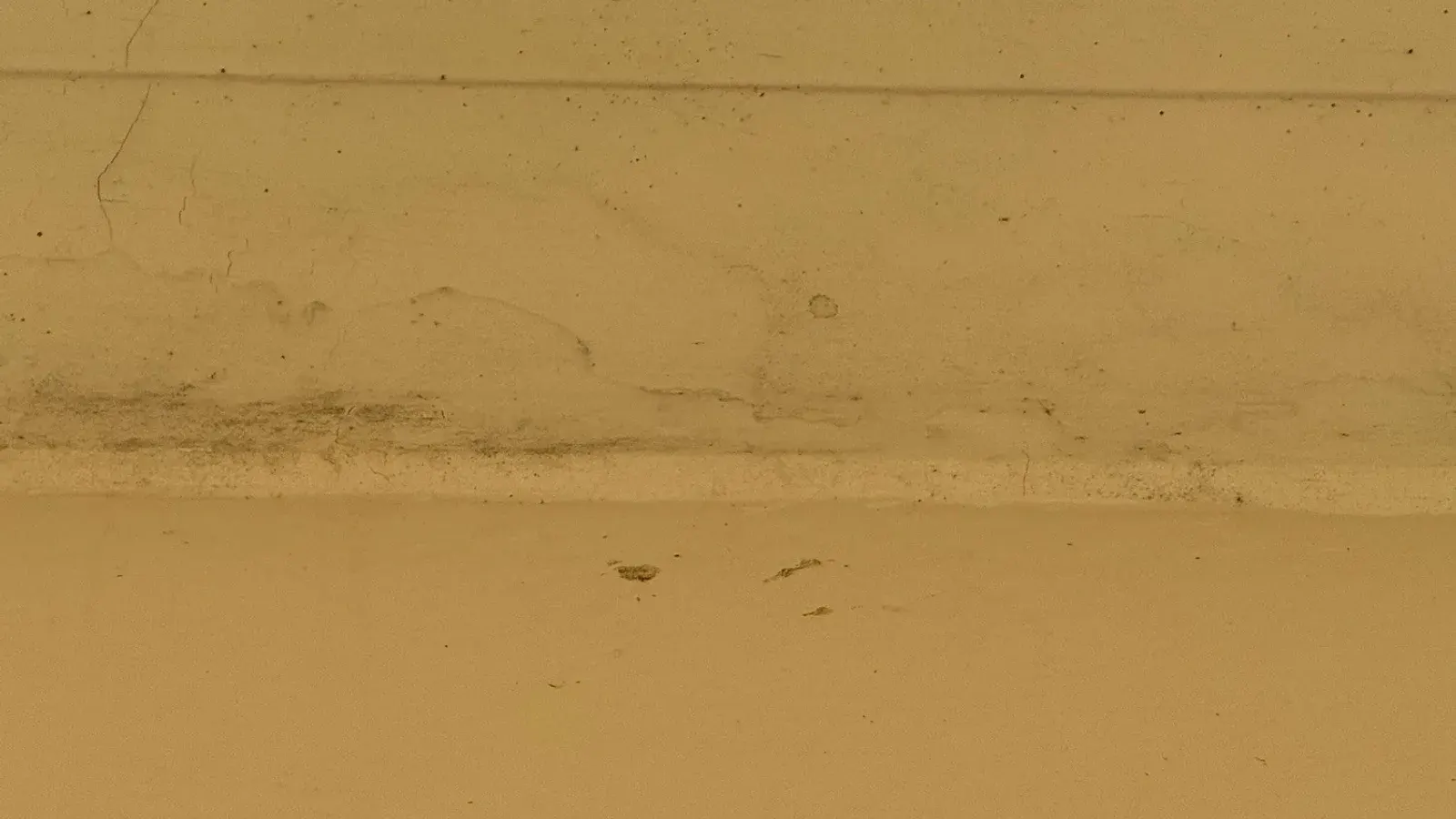 Painted surface with hairline cracks, blistered paint and a band of dark staining