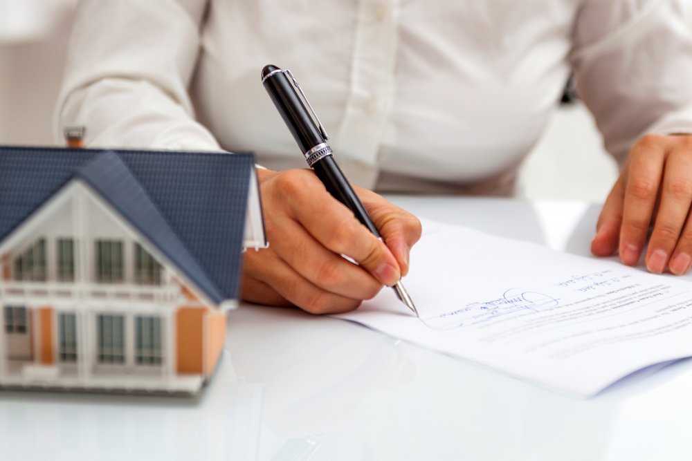 Person signing an insurance contract for a house, demonstrating the process of Insurance Claim Assessments in Geelong.